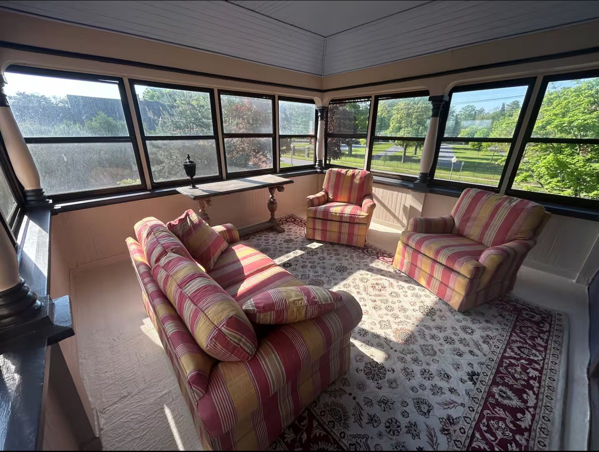 The enclosed sun porch sitting room with striped upholstered seating and views of the grounds