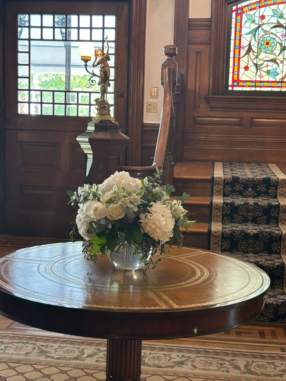 White flowers on the foyer table below the stained glass at the Union Avenue Thoroughbred Club